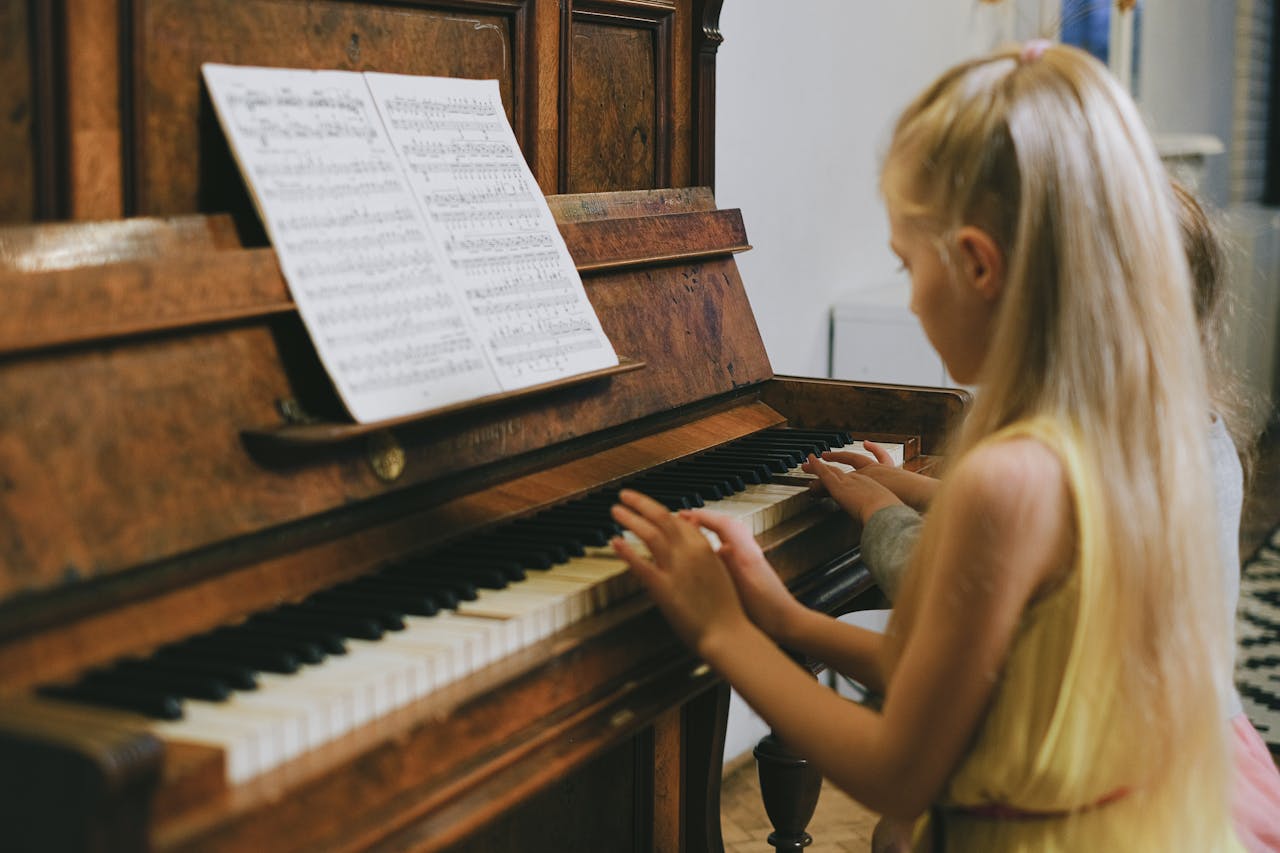 services-04 Two young girls playing piano together indoors, focused on a music sheet.